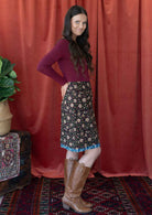 Model standing sideways wears a reversible cotton skirt in bold floral print with the pop of blue band at the base of the skirt.