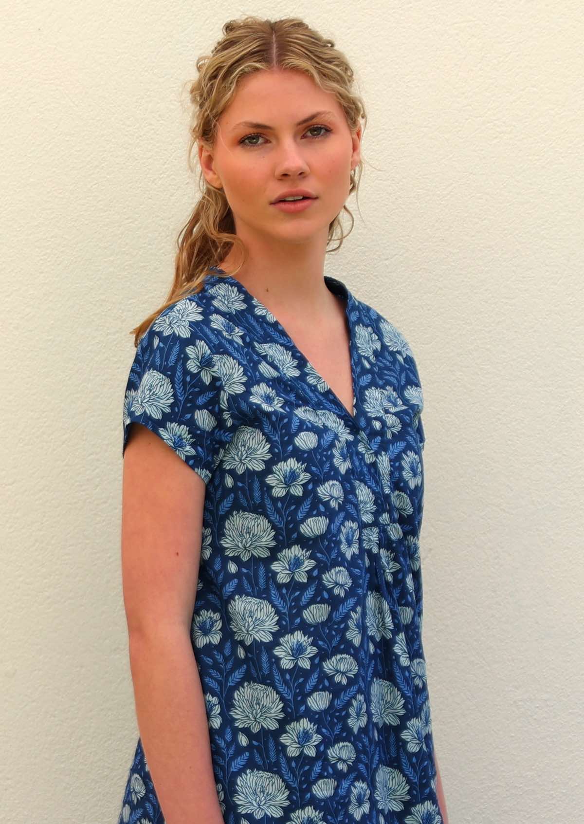 Woman with blonde hair wearing a blue cotton tunic dress with V-neckline and short sleeves in light blue and white floral print