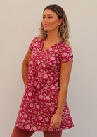 Woman stands in red based floral cotton cap sleeve tunic with top stitched V-neckline