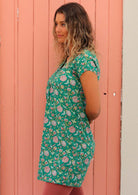 Model standing in front of pink door side on with hand behind back wearing 100 percent cotton short sleeve tunic