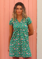 Model standing in front of pink door with one hand behind back wearing 100 percent cotton short sleeve tunic