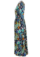 Side view of 3/4 sleeved rayon maxi dress with buttoned bodice, V-neckline and a wide shirred waistband, in a floral and peacock print on a navy base