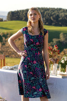 woman in front of outdoor table in retro inspired Scarlett Dress Dianthus  vibrant navy, purple, pink and aqua floral print on 100% cotton 