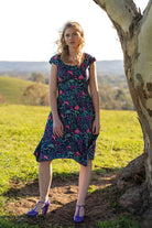 woman in retro inspired Scarlett Dress Dianthus in a  vibrant navy, purple, pink and aqua floral print on 100% cotton under gum tree