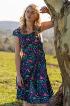 woman in retro inspired Scarlett Dress Dianthus in a  vibrant navy, purple, pink and aqua floral print on 100% cotton under gum tree with arm up