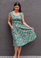 Model wearing green 100 percent cotton scoop neck retro dress with one hand in pocket and displaying the dress's skirting with other hand 