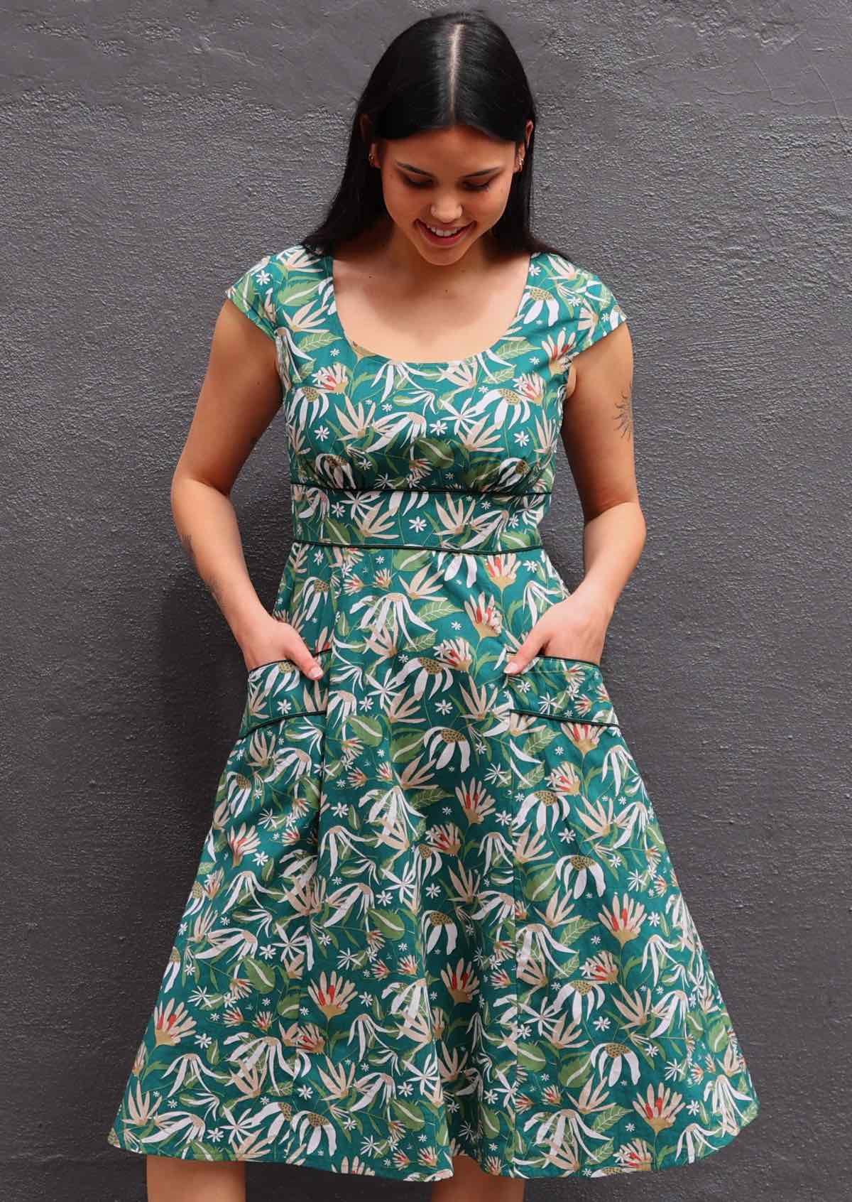 Model looking down wearing green 100 percent cotton scoop neck retro dress with both hands in pockets 