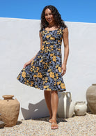 Model wears 100% cotton knee length retro style dress in black with yellow, blue and grey florals