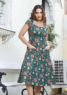 Model with both the hands in pockets of retro style cotton dress with pink, cream and orange floral print on deep green base