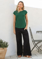 Woman wearing a 100% rayon forest green shell t-shirt with plain black pants in an outdoor setting