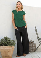 Woman leans on wall wearing a 100% rayon forest green shell t-shirt and plain pants