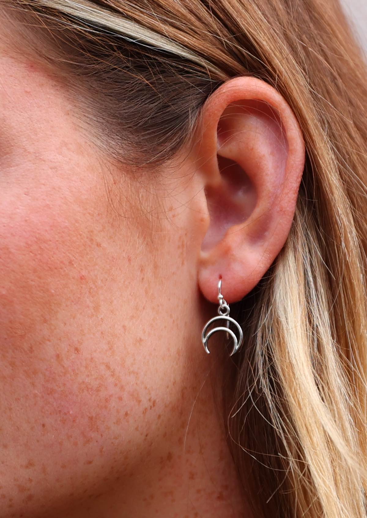 Woman wears sterling silver crescent moon cutout earring, hanging from a wire hook