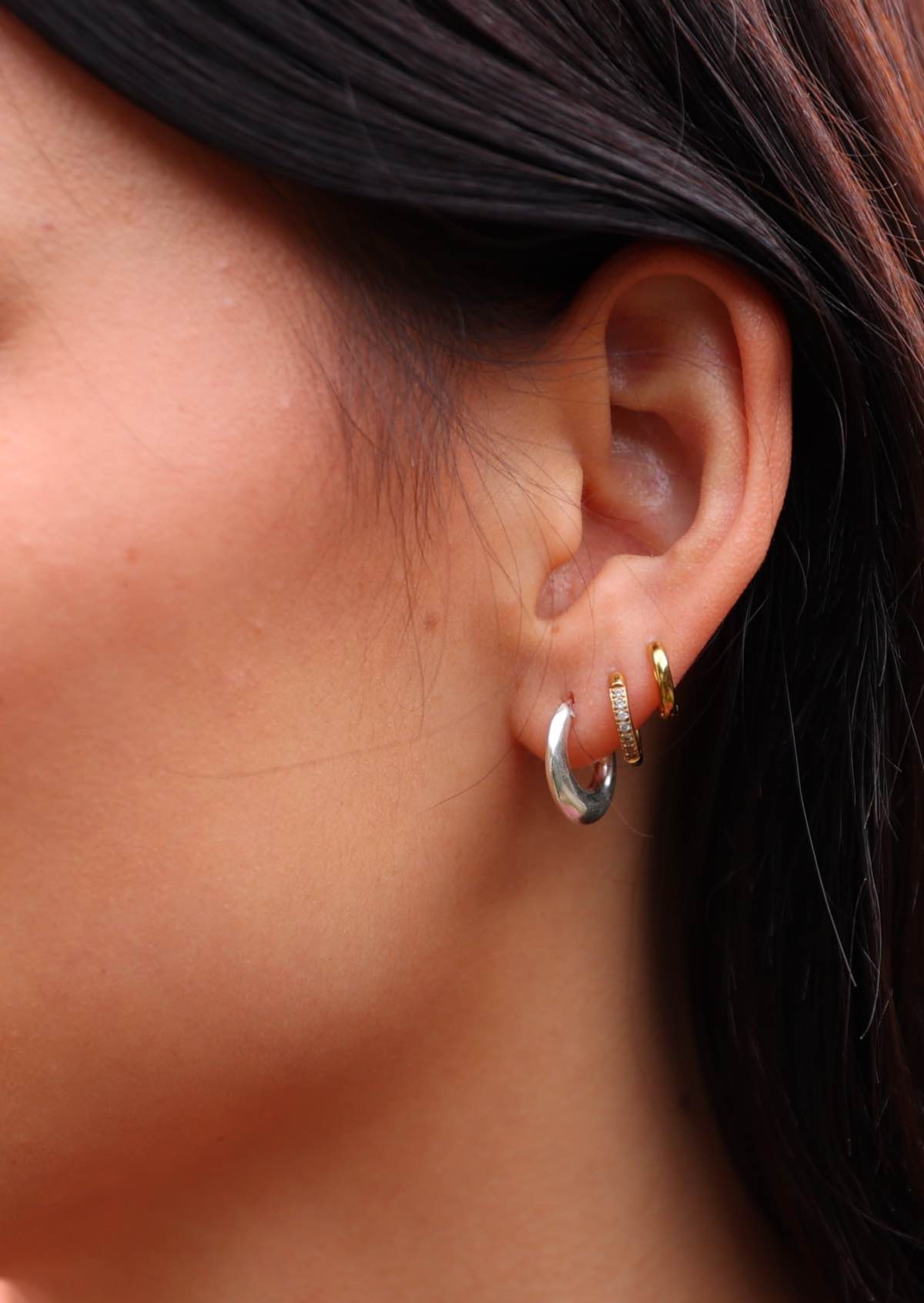 Woman wears sterling silver chunky hoops huggie earrings with her own small gold hoops