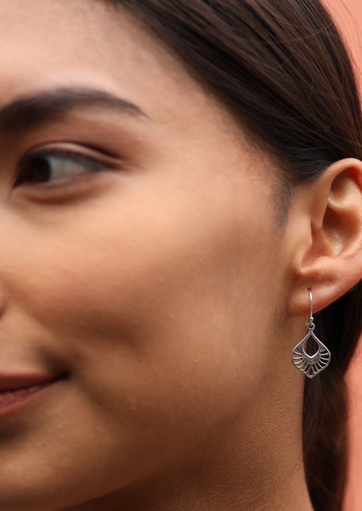 Woman wears silver nouveau style cutout earrings with a wire hook