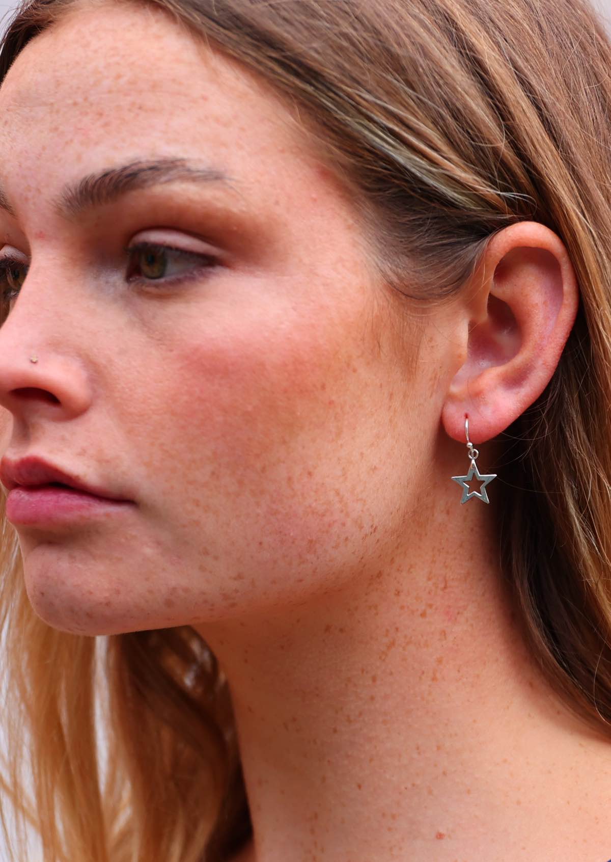 Woman wears silver five point star hook earrings