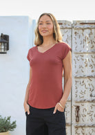 Woman wearing a 100% rayon terracotta v-neck T-shirt and black pants standing in front of a textured wall.