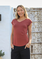 Woman wearing a 100% rayon terracotta V-neck T-shirt and black pants, standing against a white wall.