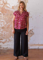 Full length image of model in cotton floral top with bright red base paired with black cotton pants