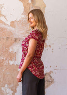 Woman stands sideways in 100% cotton cap sleeve floral print top that is longer at the back