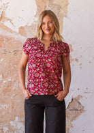 Woman poses in cotton floral print top on a bright red base, featuring a V-neckline and mandarin collar