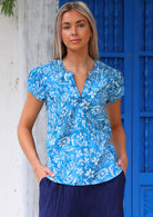 Model wears cotton blue floral print short sleeve top with V-neckline and elastic ruching at the front of the shoulders