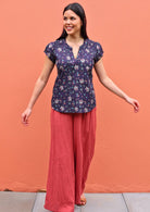 Model wearing capped sleeve cotton blouse in an Indian floral print paired with wide leg coral coloured pants