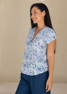 woman wearing a white based blue floral print, short sleeve cotton top.
