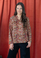 Model wears lightweight, cotton long sleeve top with keyhole cutout, in a earthy red based floral print.