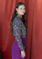 Model standing sideways wears a lightweight floral printed, shirt style cotton top in dark purple.