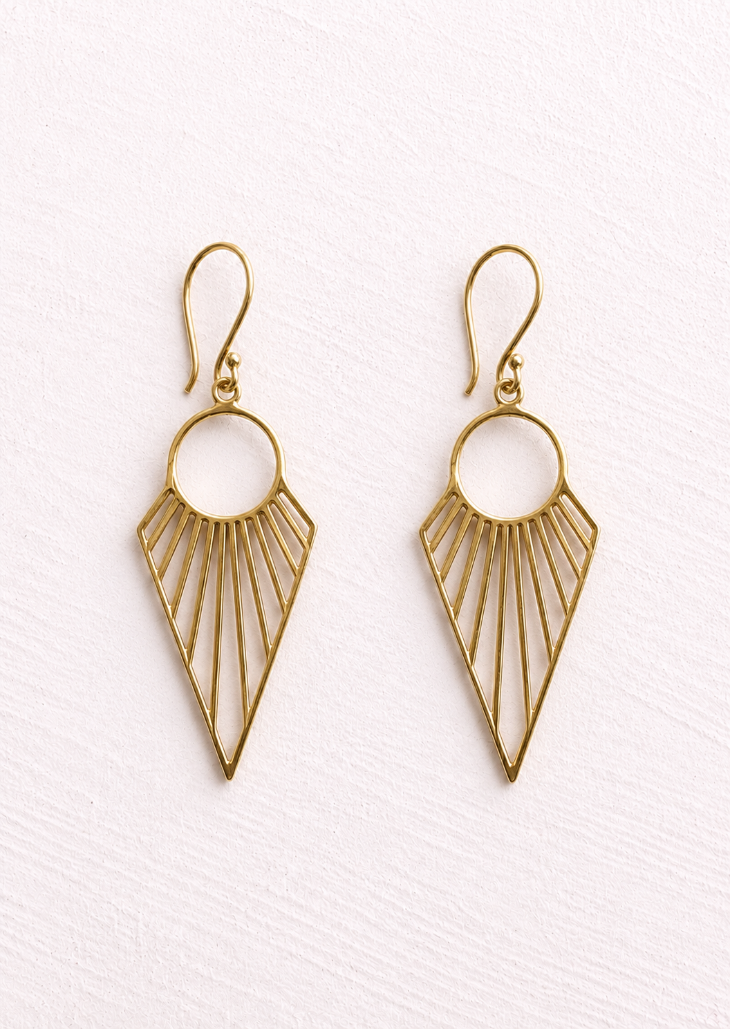 A pair of gold-tone geometric dangle earrings with a circular top and a fan-like radiating line design, shown on a textured white background.