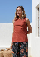 Woman standing outdoors wears a 100% cotton plain sleeveless top in rust with side bust darts and trim detailing at high round neckline and armholes