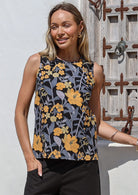 Woman wearing a sleeveless retro floral cotton top with round neckline in front of a rustic wooden window 