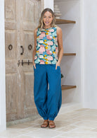 Woman wearing a pastel sleeveless top and blue pants standing in a room with wooden doors.
