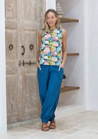 Woman wearing a pastel sleeveless top and blue cotton harem pants standing with hands in pockets