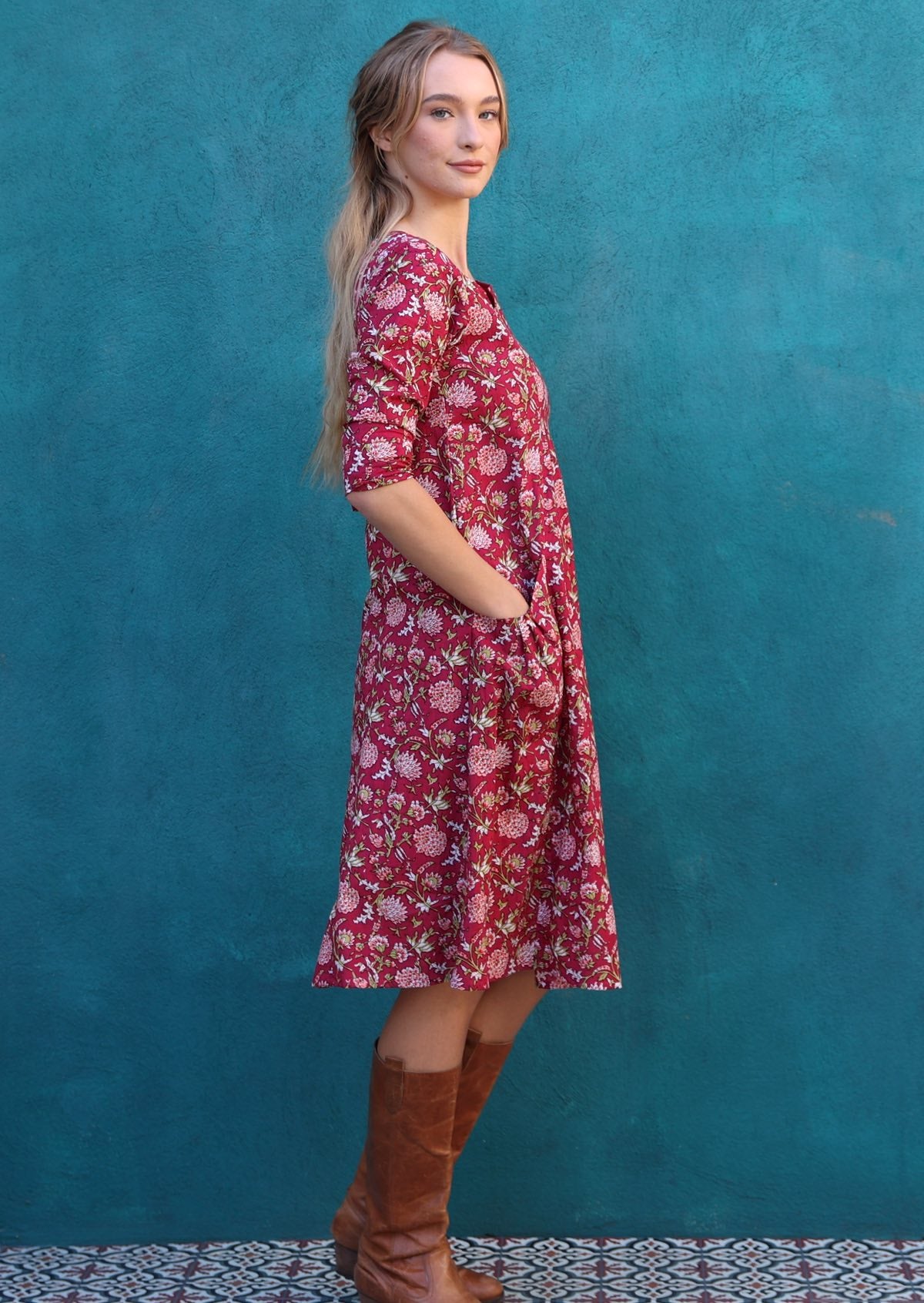Model wears 100% knee length cotton dress with hints of pink, white and green on red base 