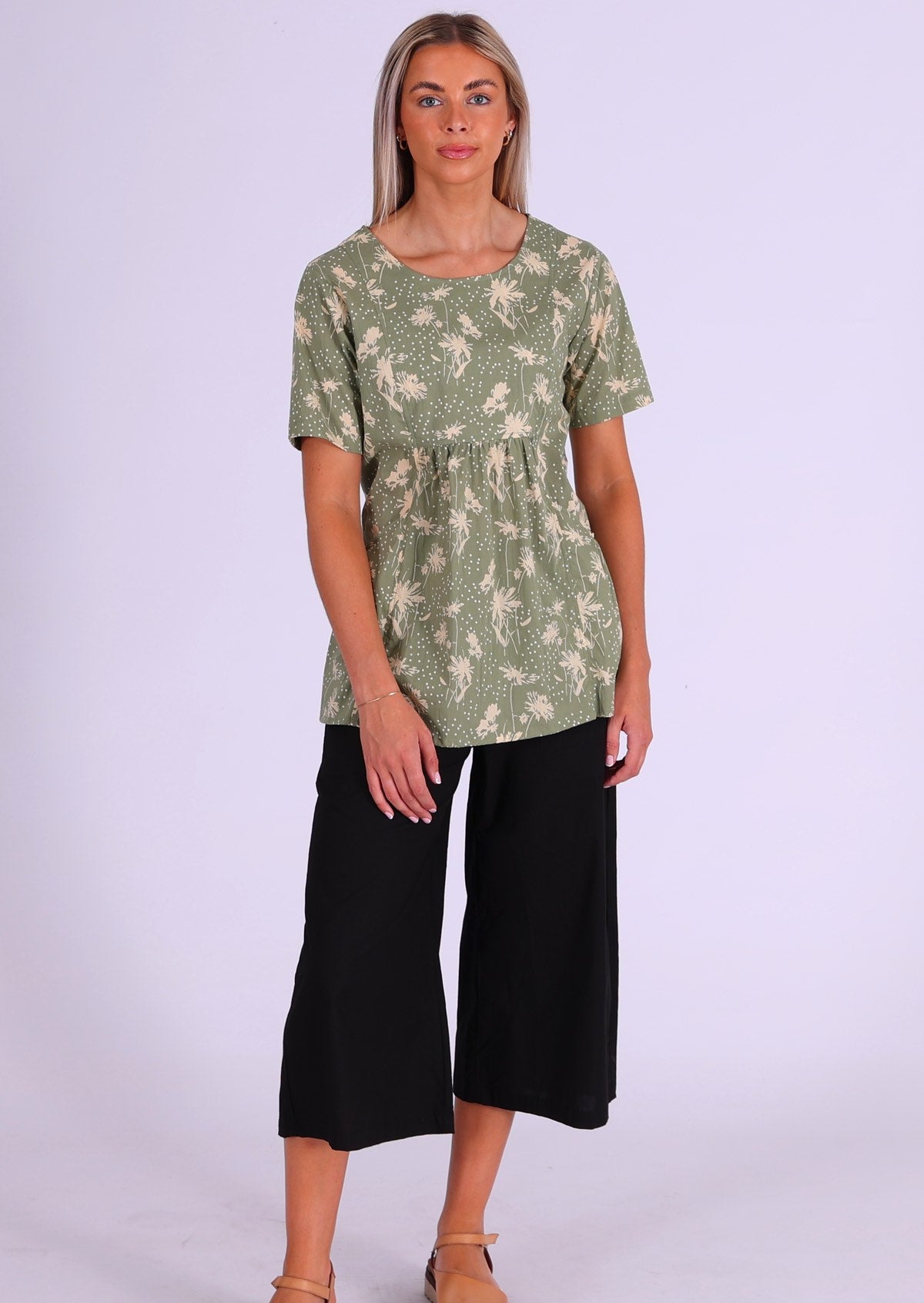 Full length photo of woman in cotton relaxed fit top with short sleeves and pockets, paired with black cotton 3/4 pants