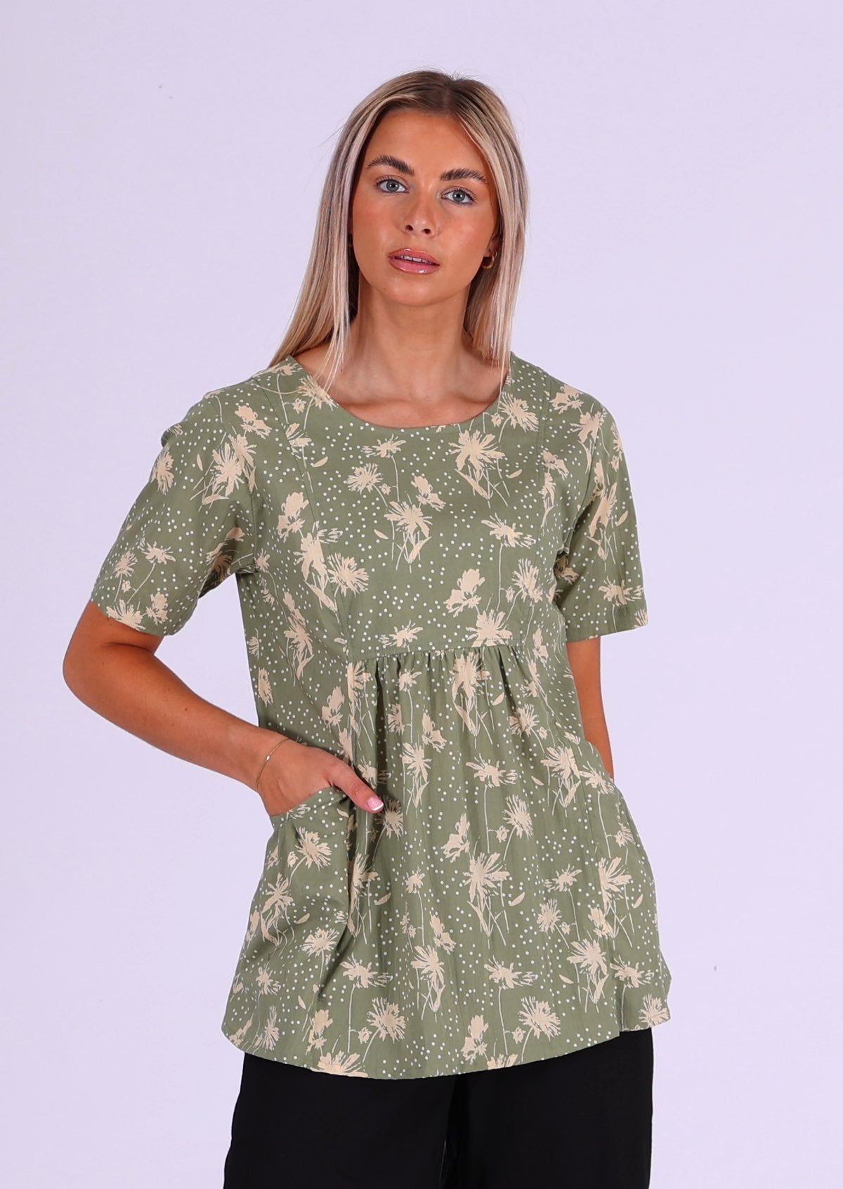 Model wears cotton relaxed fit top in cream floral print on pale green base with hand in pocket