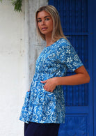 Woman stands sideways in cotton relaxed fit short sleeve top with gathers under the bust and generous pockets