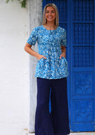 Full length photo of woman in cotton relaxed fit top with short sleeves and pockets, paired with dark blue cotton pants