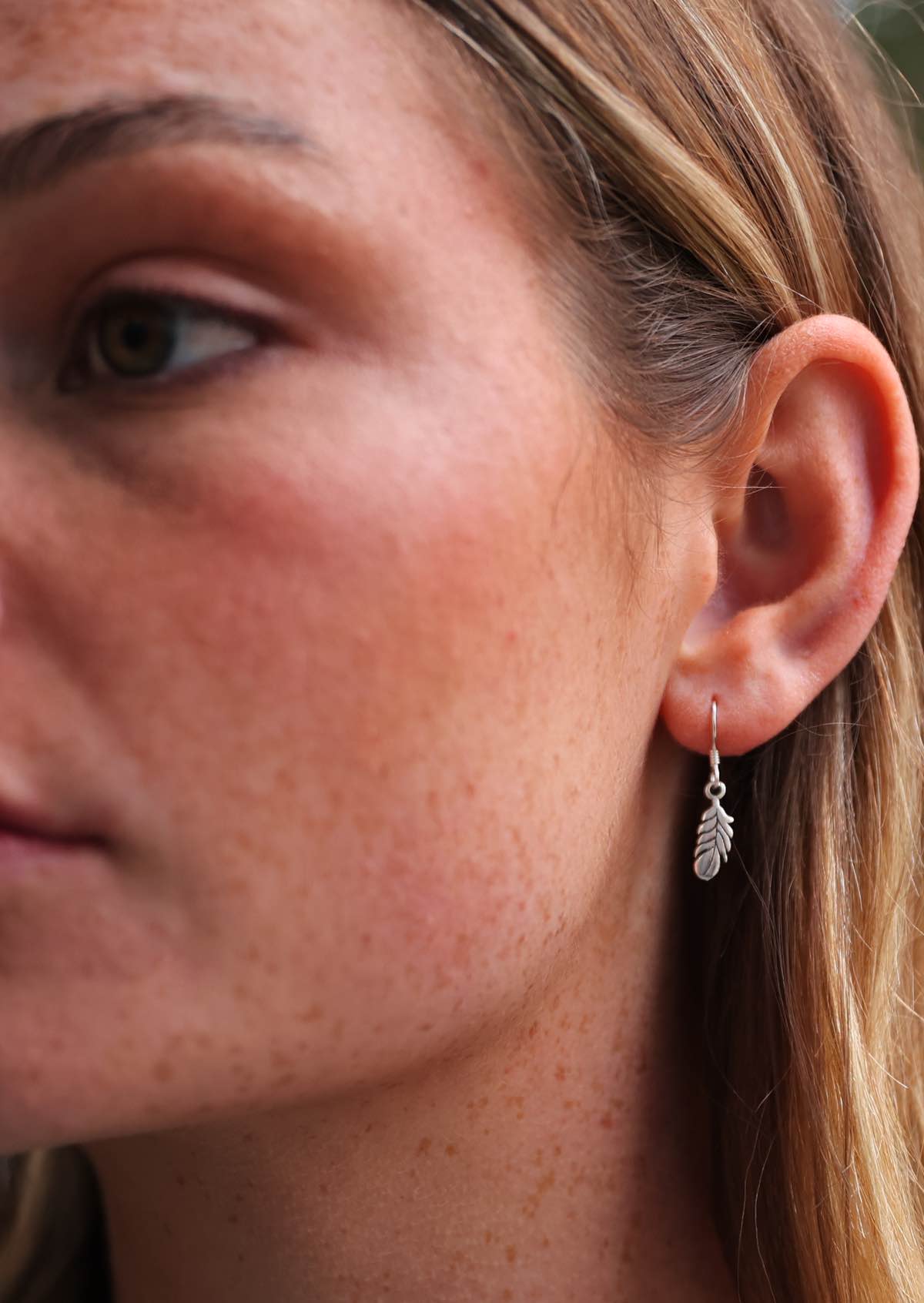 Woman wearing Tiny Silver Feather Earrings, suspended on wire hooks