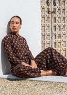 Woman sits in long sleeve cotton tunic with matching print harem pants, both with  red floral motif print.
