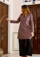 Model standing near wooden doors wears lightweight 100% cotton long sleeved tunic in beautiful purple based floral print.