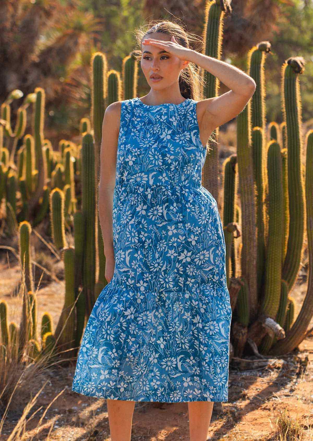 Woman in blue 100% cotton floral dress with hand raised to shade eyes from the sun