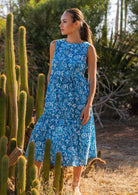 Woman in blue 100% cotton floral dress with hand in pocket behind cacti