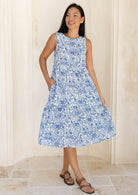 woman wearing a white based blue floral print cotton dress with her hand in pocket.