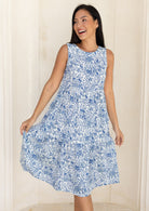 woman wearing a white based blue floral print cotton dress against a white background.