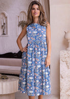 Woman wearing a mid length, sleeveless blue floral cotton dress in an elegant room.