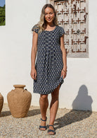 Woman in a knee length navy blue cotton  dress with cap sleeves, standing in front of a white wall with decorative elements