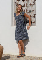 Woman posing in front of the white wall wears 100% cotton navy blue floral motif printed dress with cap sleeves and round neckline