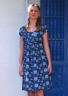 Model wears short sleeved cotton dress with pin tucks across front of bodice in blue floral print